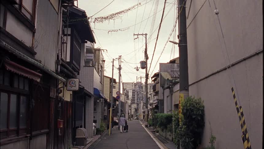 Woman pushes baby carriage along narrow road between buildings