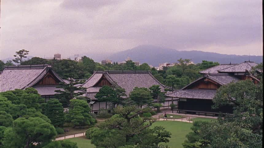 Two people walk by buildings near an open area
