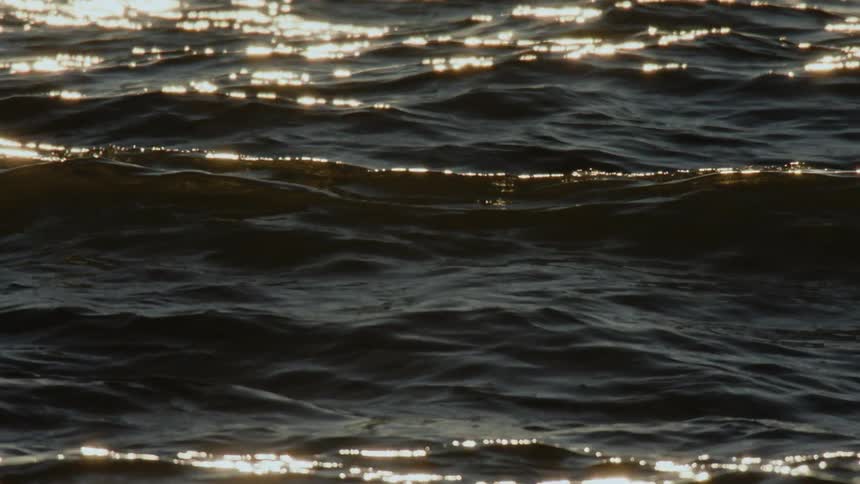 Rolling ocean waves in slow motion with evening sunlight flickering in reflections