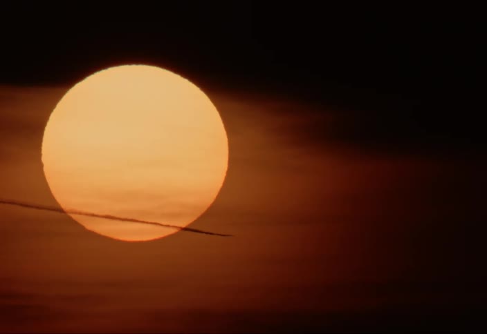 The evening reddened sun in the sky as a jet stream passes through