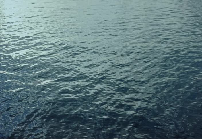 A surface of sea water with calm ripples in the evening and reflections