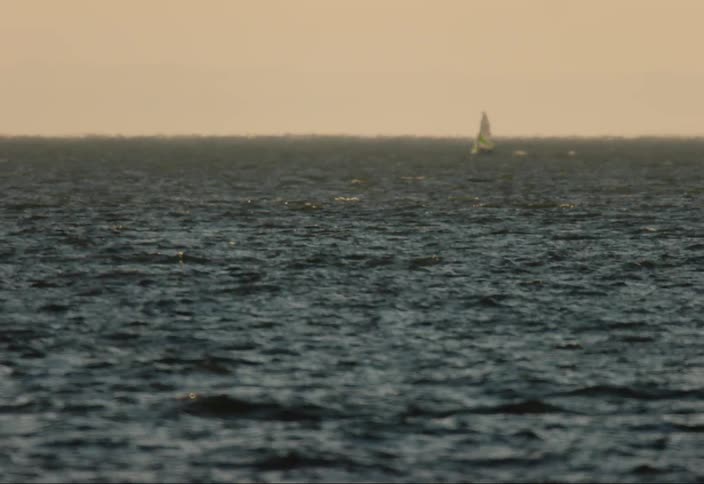 A sailboat moves across the open ocean with distant heat waves
