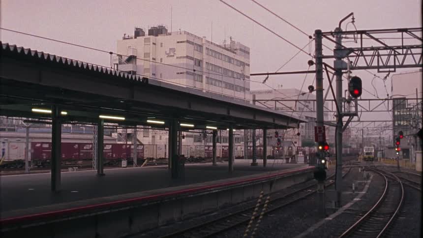 A freight train travels on tracks passing a passenger train platform in a city
