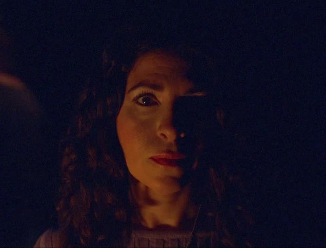 An expressionless woman completely still while shapes and lights move all around her