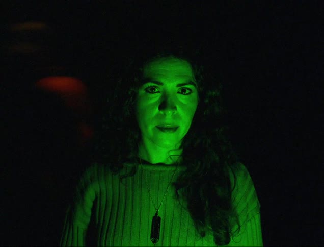 A woman is standing in a dark environment while a red light hits her body and then turns into green light