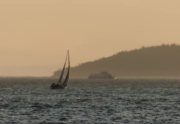 People sailing in a sailboat on the ocean as a boat passes by in the background