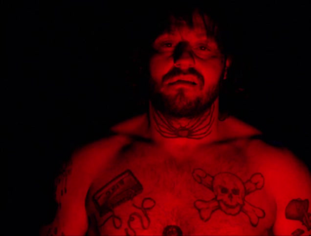 A red light shining on a shirtless man with tattoos on his neck and chest