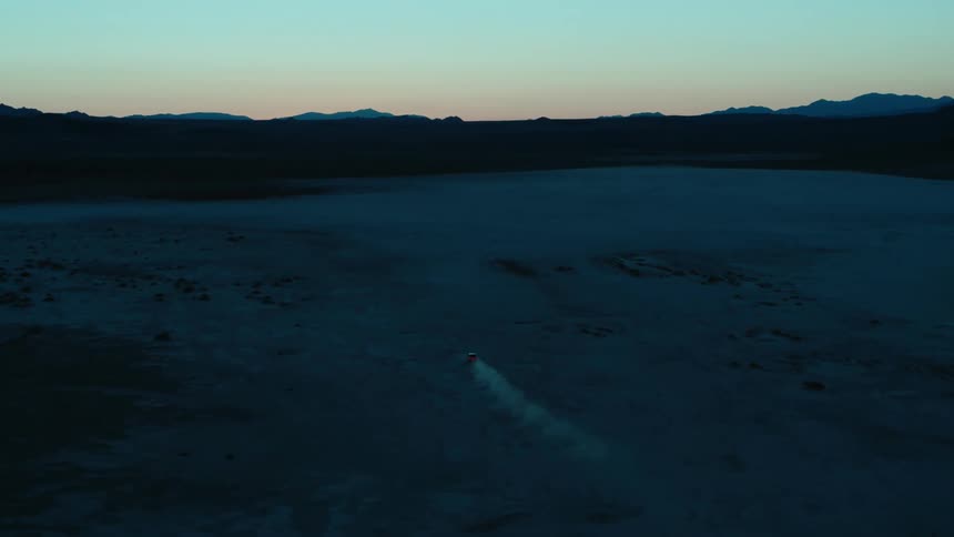 A truck drives through the desert at sunset