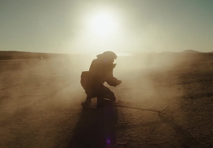 A silhouette of a man using a metal detector out in the desert