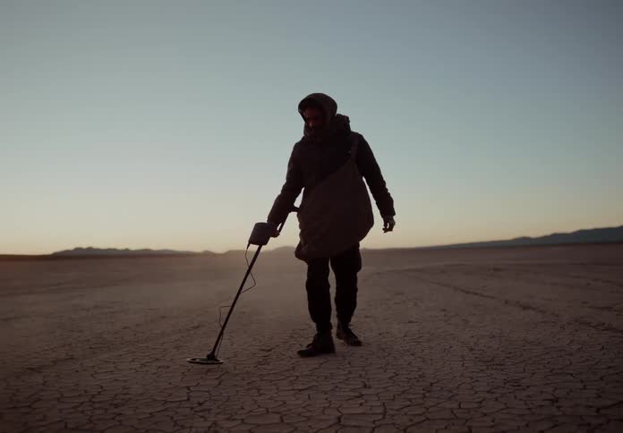 A man uses a metal detector in a desert