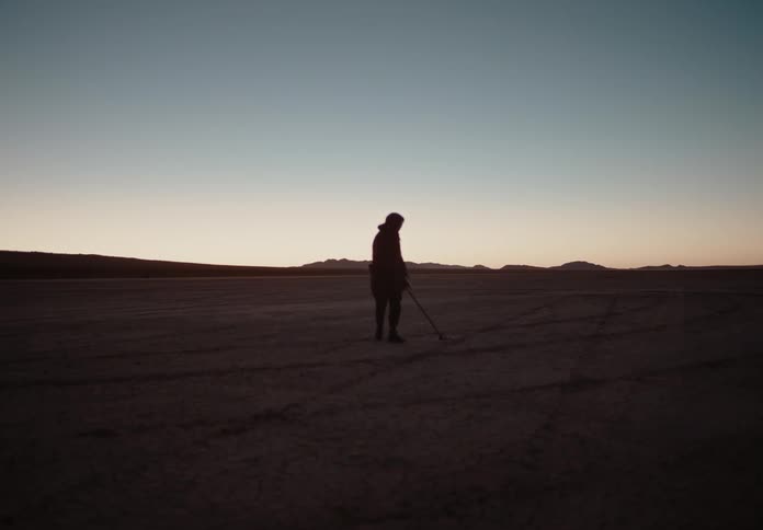 A man looks for something with a metal detector in a desert