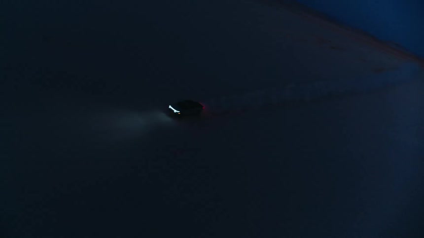 Car drives on a dirt road through the wilderness with their headlights on after sundown