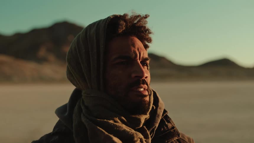 A black man stares into the distance in a desert