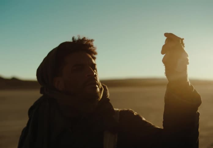 Man enjoying a metallic object in his hands while standing on dry desert ground with the sun strong on the horizon
