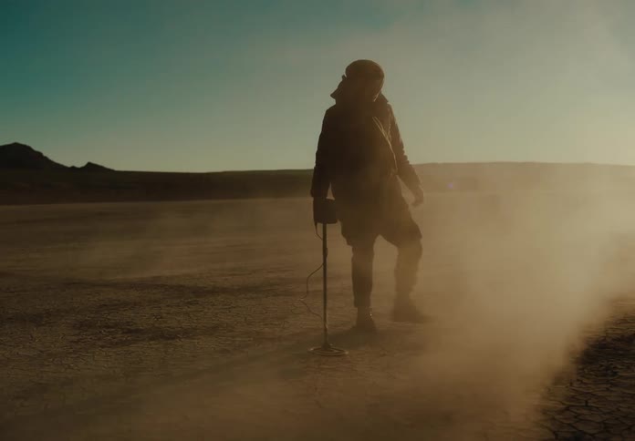 A man is using a metal detector in the desert