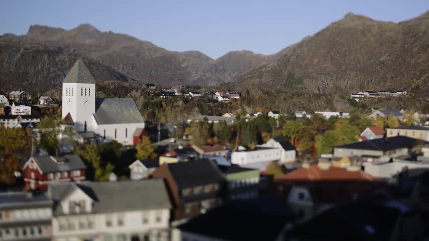 A white church in a town with small houses and lots of trees around it and behind it there are huge mountains