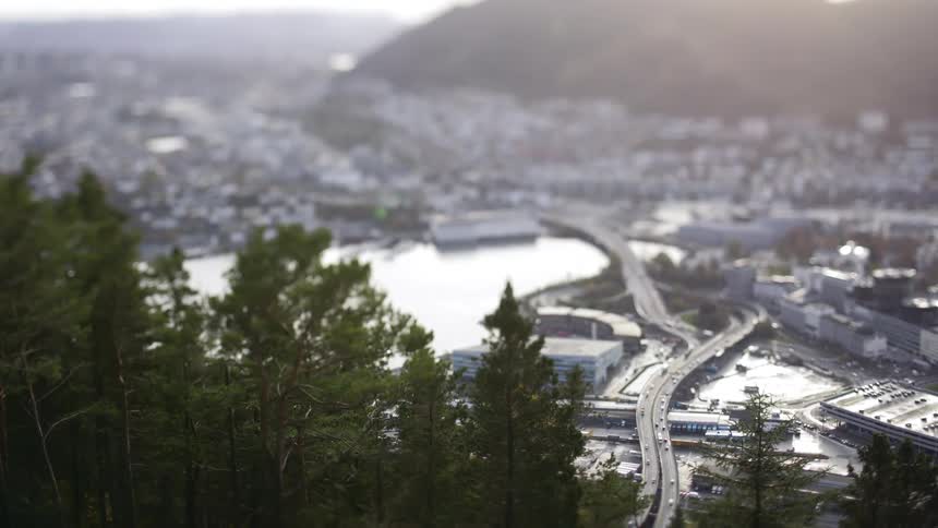 A tilt shifted cityscape viewed from a hill with buildings and roads below