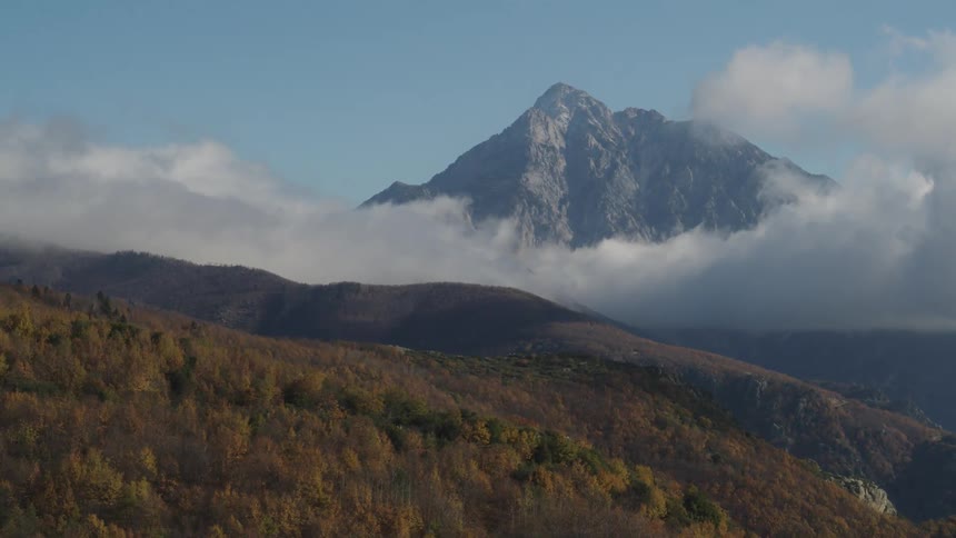Landscape of mountain ranges with forests and clouds around on a blue sky day