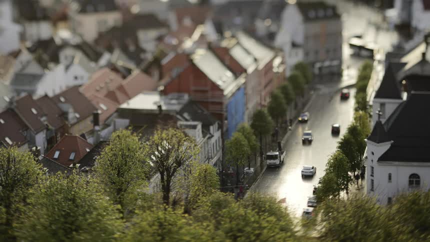 A street with cars and people passing by in a small town with lots of trees