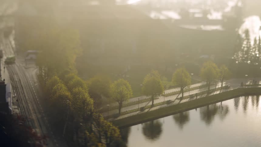 View from above of a city with a train passing by and vehicle traffic next to a lake with pedestrians in great timelapse