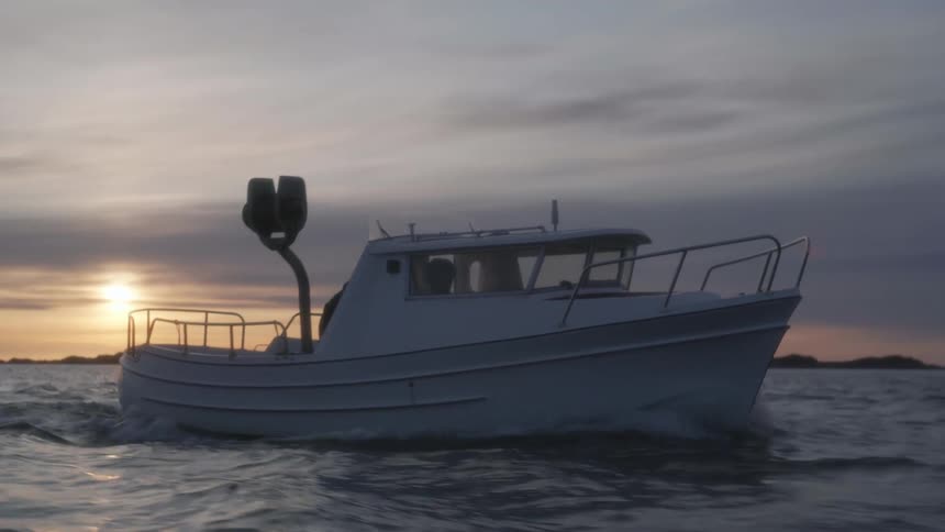 Small boat traveling through the sea in the late afternoon with the sun setting on the horizon