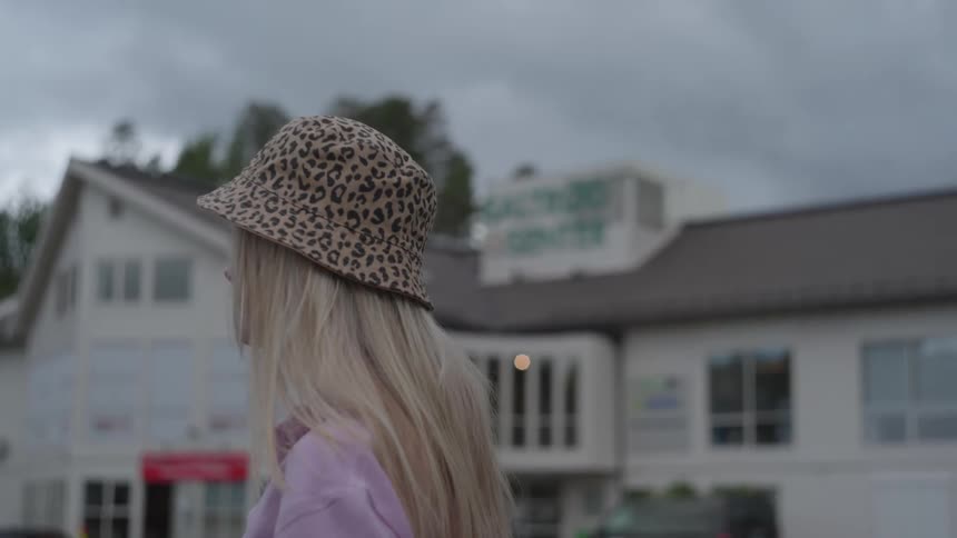 Blonde woman wearing a hat while outdoors with a commercial store next door on a cloudy day