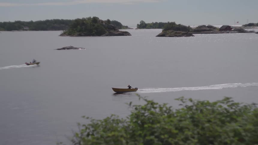 Two small motor boats traveling through the sea with rocks and islands around