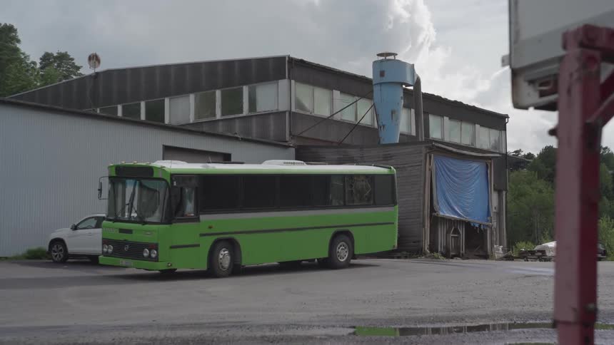 A green bus parked outside an industrial building under a cloudy sky