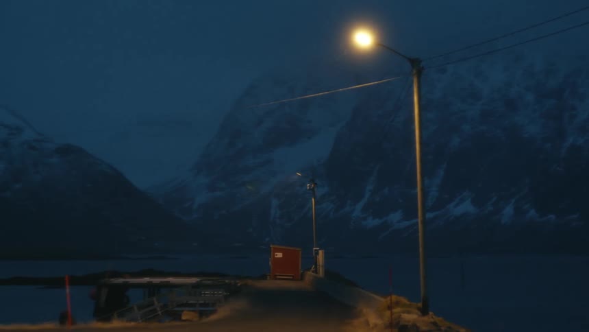 Lights flashing on platforms in the middle of the sea next to mountains covered in snow at night