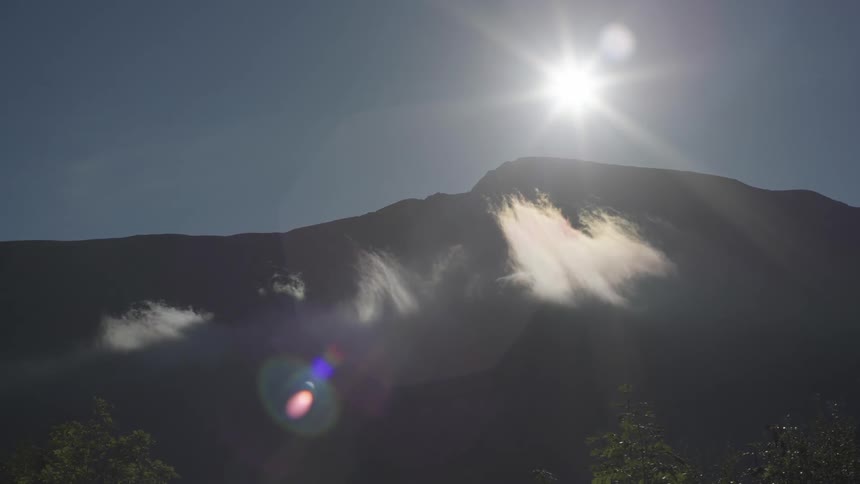 A view of a mountain with sun above it