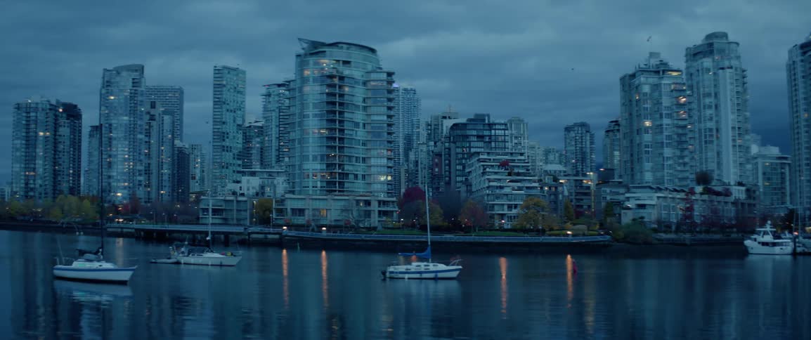 Sailboats anchored in still water at dusk in front of seafront buildings