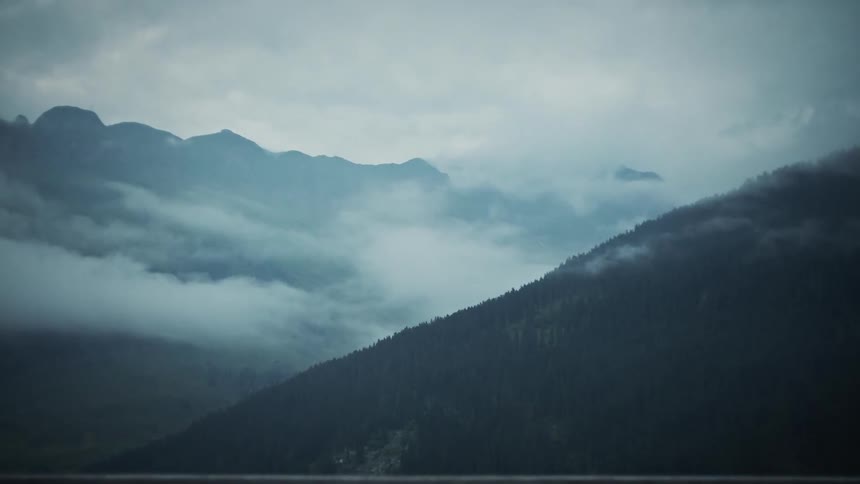 Panorama of mountain ranges with clouds around and vast coniferous vegetation