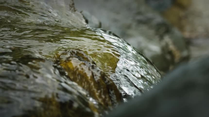 Crystal clear water flows swiftly over a cluster of rocks in a stream