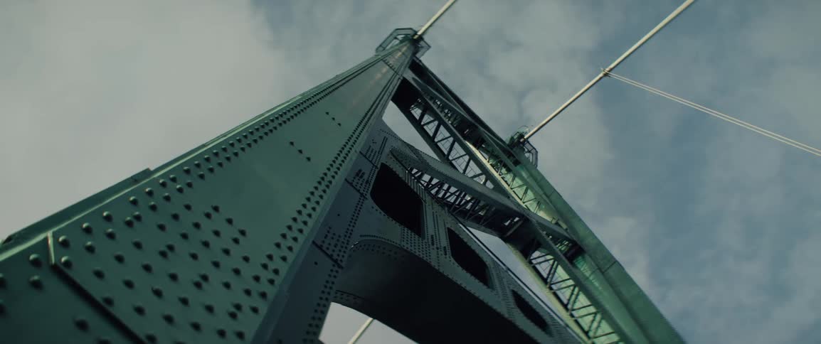 Upward view of the green bridge tower with suspension cables