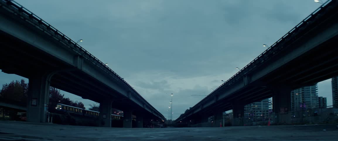A train passing on the tracks that are under two huge viaducts on a cloudy city morning