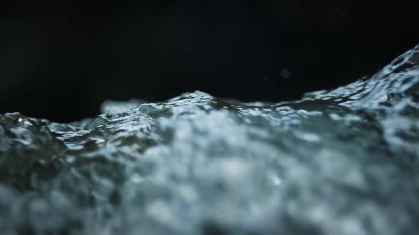 Water flows rapidly over a vertical drop spraying droplets into the dark