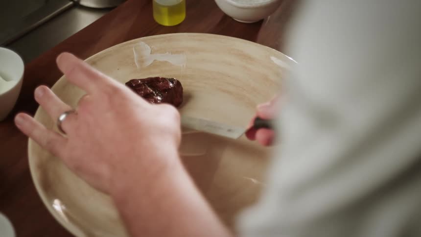 A mans hands are shown plating a small steak with a knife