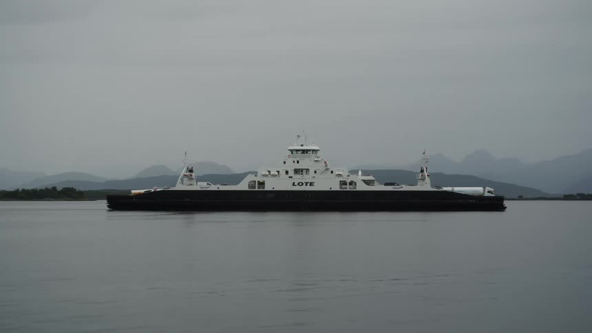 A large white ship carrying vehicles passing through a lake with calm water