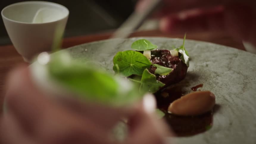 A cook is using tweezers to place garnish on a dish