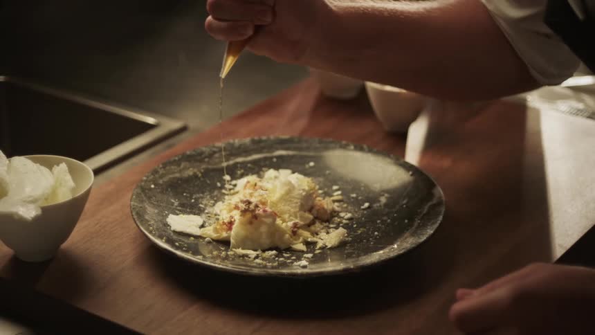 A persons hand placing honey on a plate with a dessert
