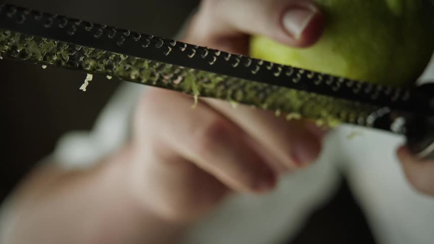 A persons hand zesting the lemon on a kitchen utensil in slow motion