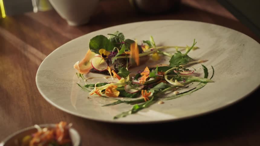 Close on a white porcelain plate and a persons hand pouring salad