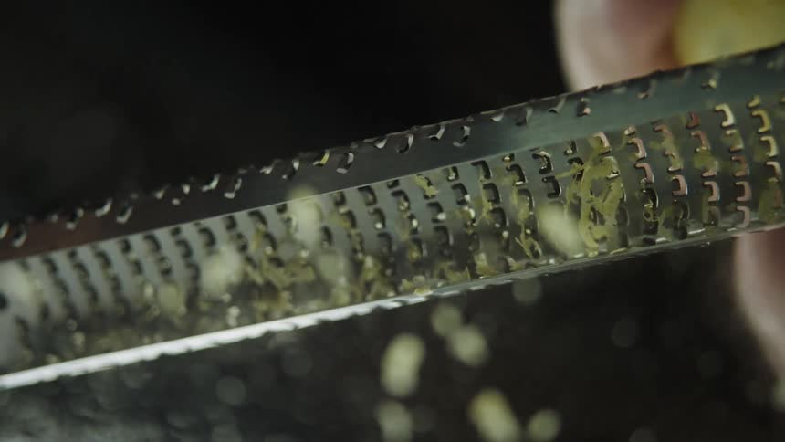 A persons hand shaving a lemon into the grater