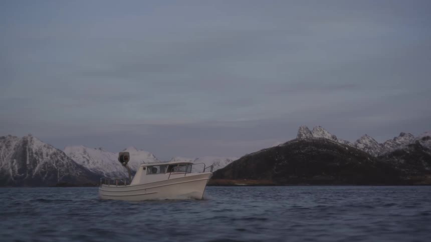 Small boat traveling through the sea with snowcovered mountains around