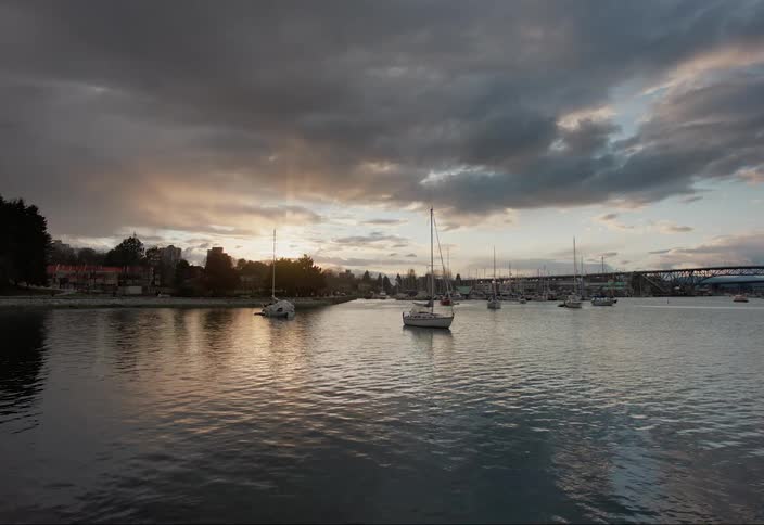 Several sailboats floating in a marina as the sun sets in the distance