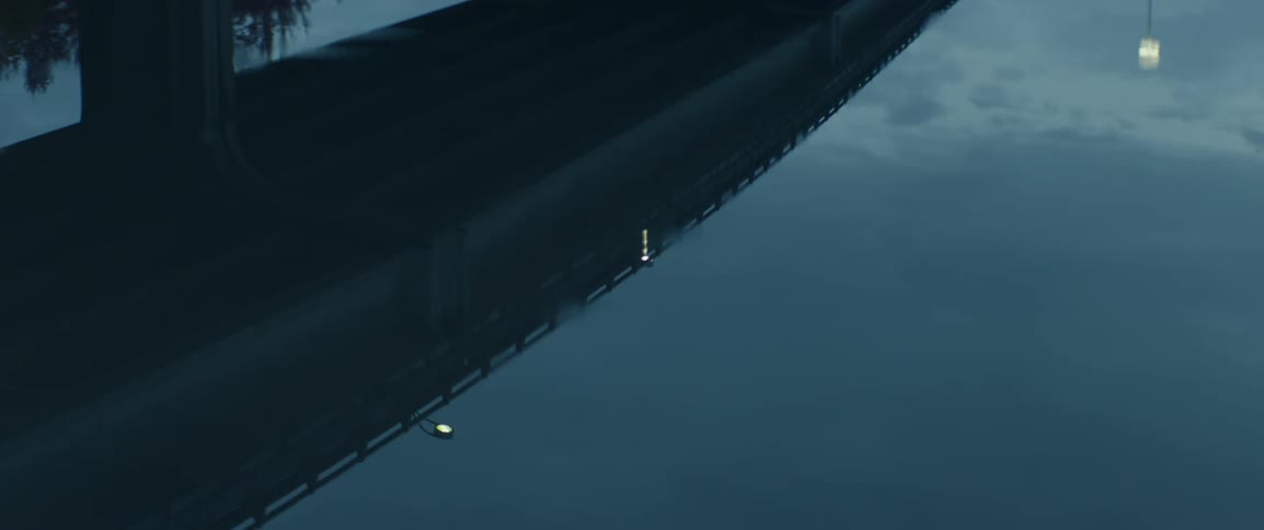 Raindrops disturbing the reflection of a roadway in a puddle at dawn