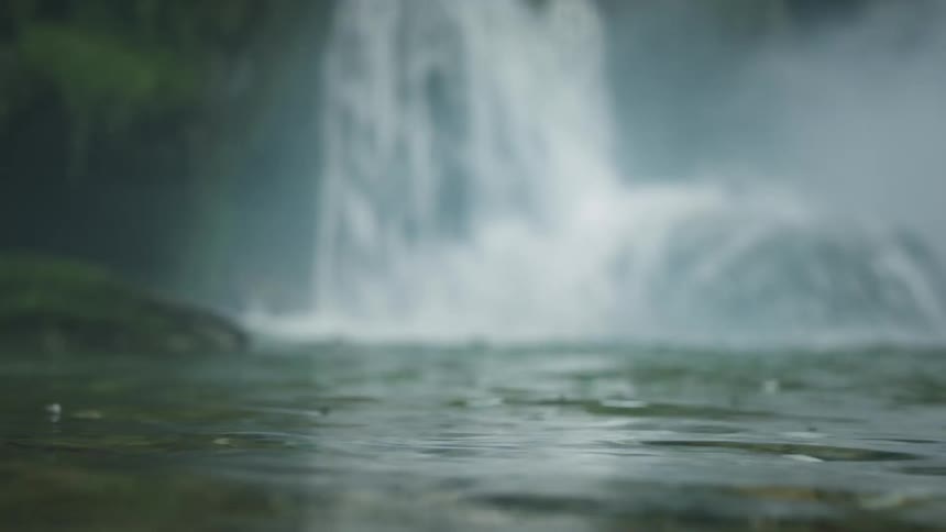 A water surface that is moving randomly due to a waterfall behind it and is out of focus