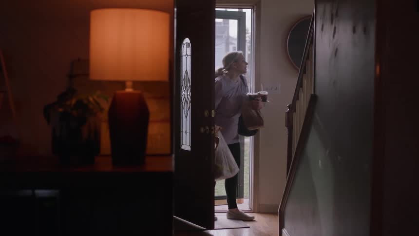 A woman is entering a room carrying grocery bags