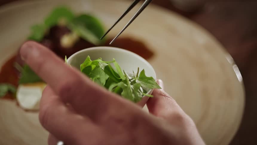 A cook is plating food using tweezers to put garnish on a dish
