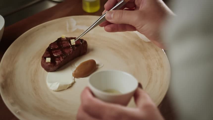 A person plating a grilled steak on with condiments